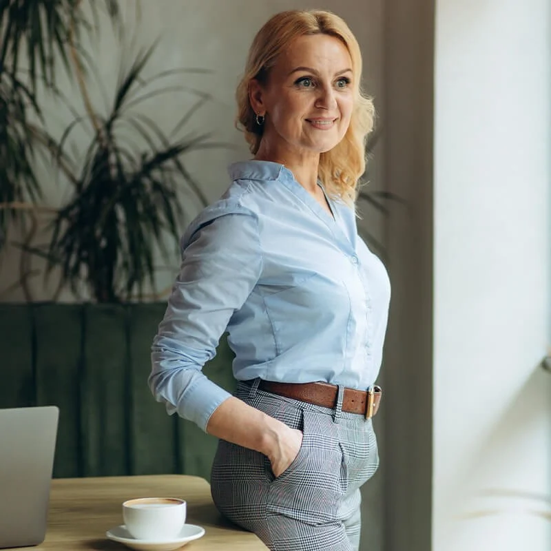Confident woman enjoying clear vision after retinal care treatment - IC Retina Smiling middle-aged woman standing by café table with coffee, representing improved eyesight after IC Retina care - IC Retina